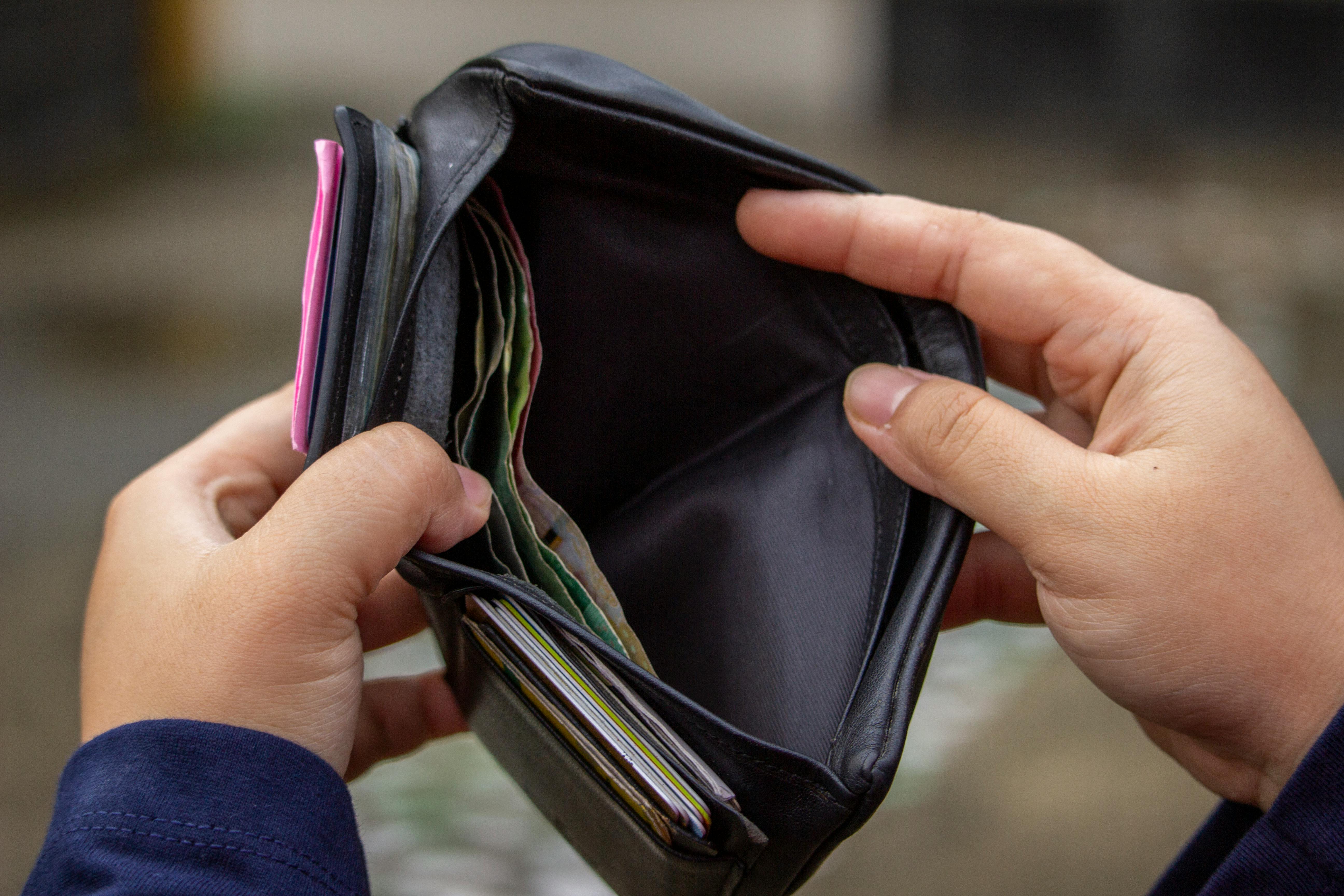 Hands opening a black wallet stuffed with cards and cash