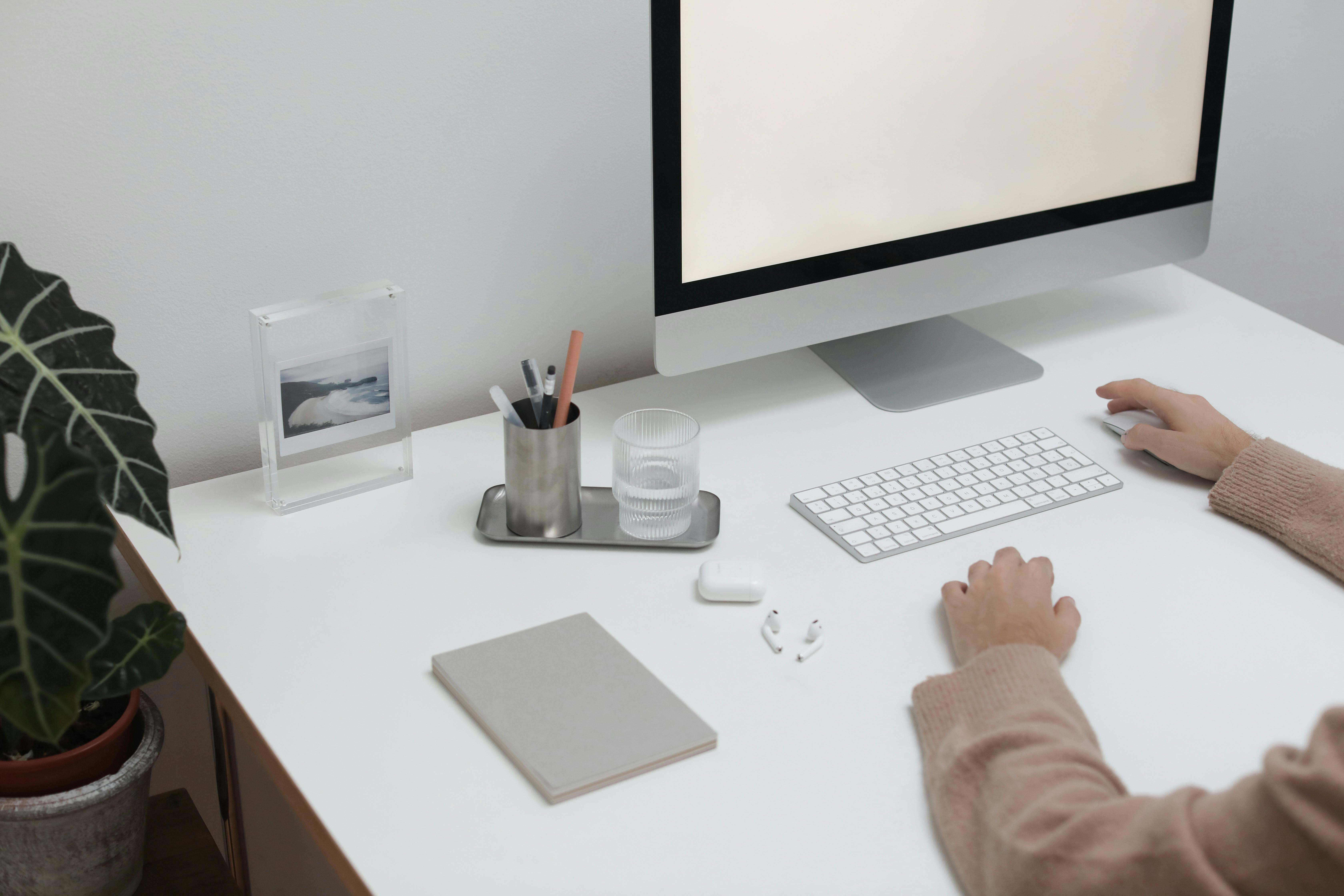 Clean minimal home office desk with iMac, keyboard, plant, and notebook