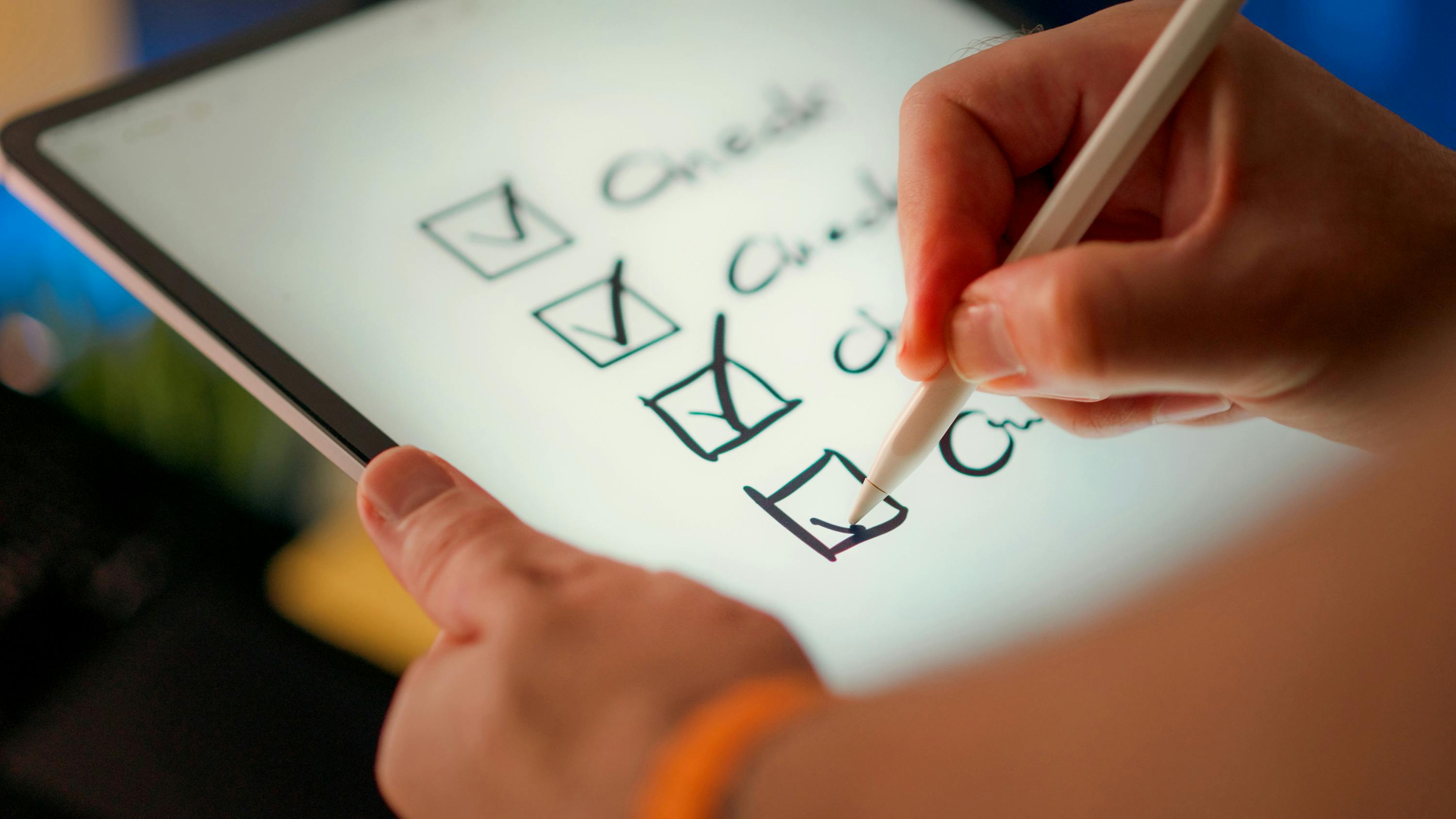 Hands holding a tablet and stylus checking off items on a digital checklist