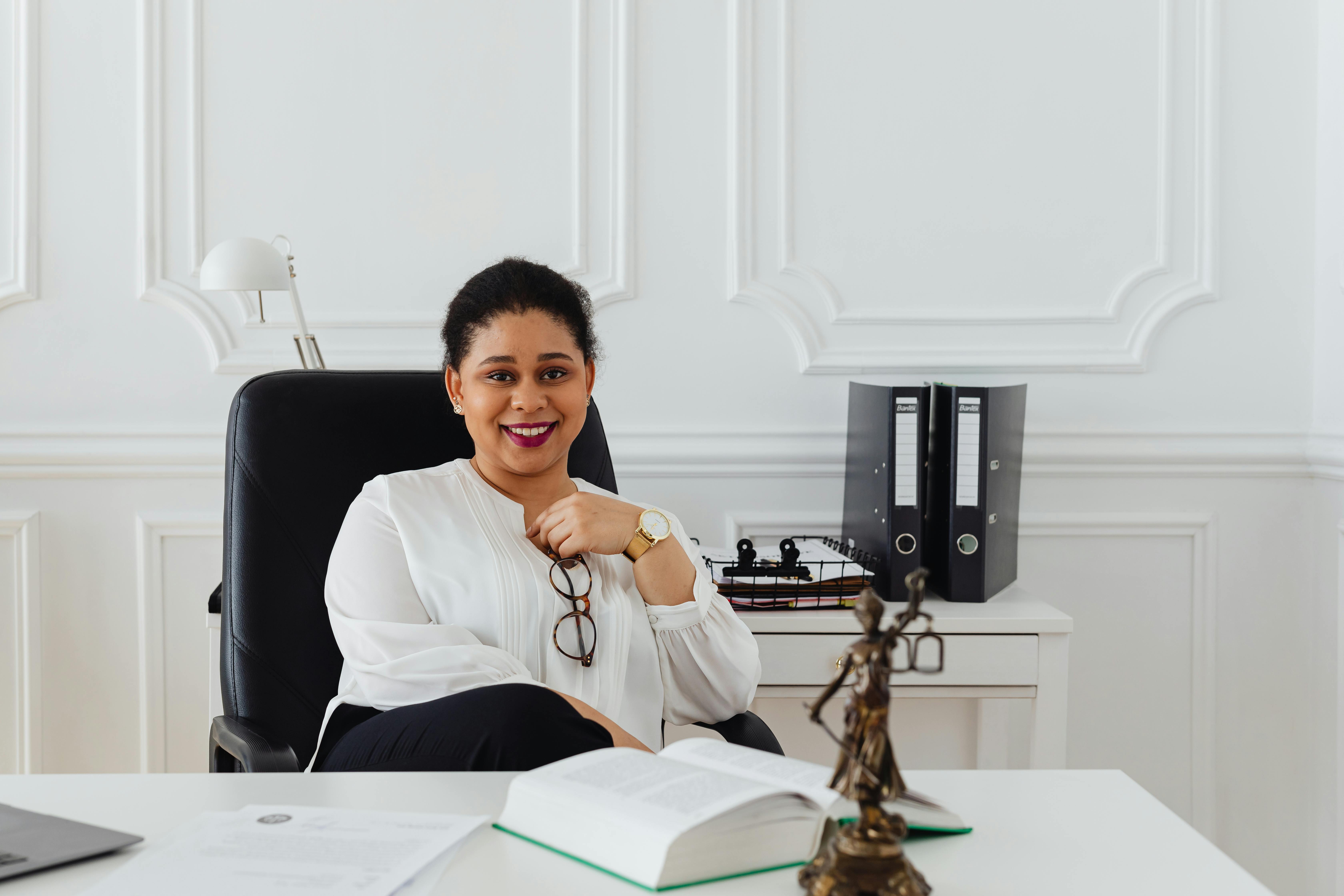 Female attorney smiling at her desk with a Lady Justice statue and legal files