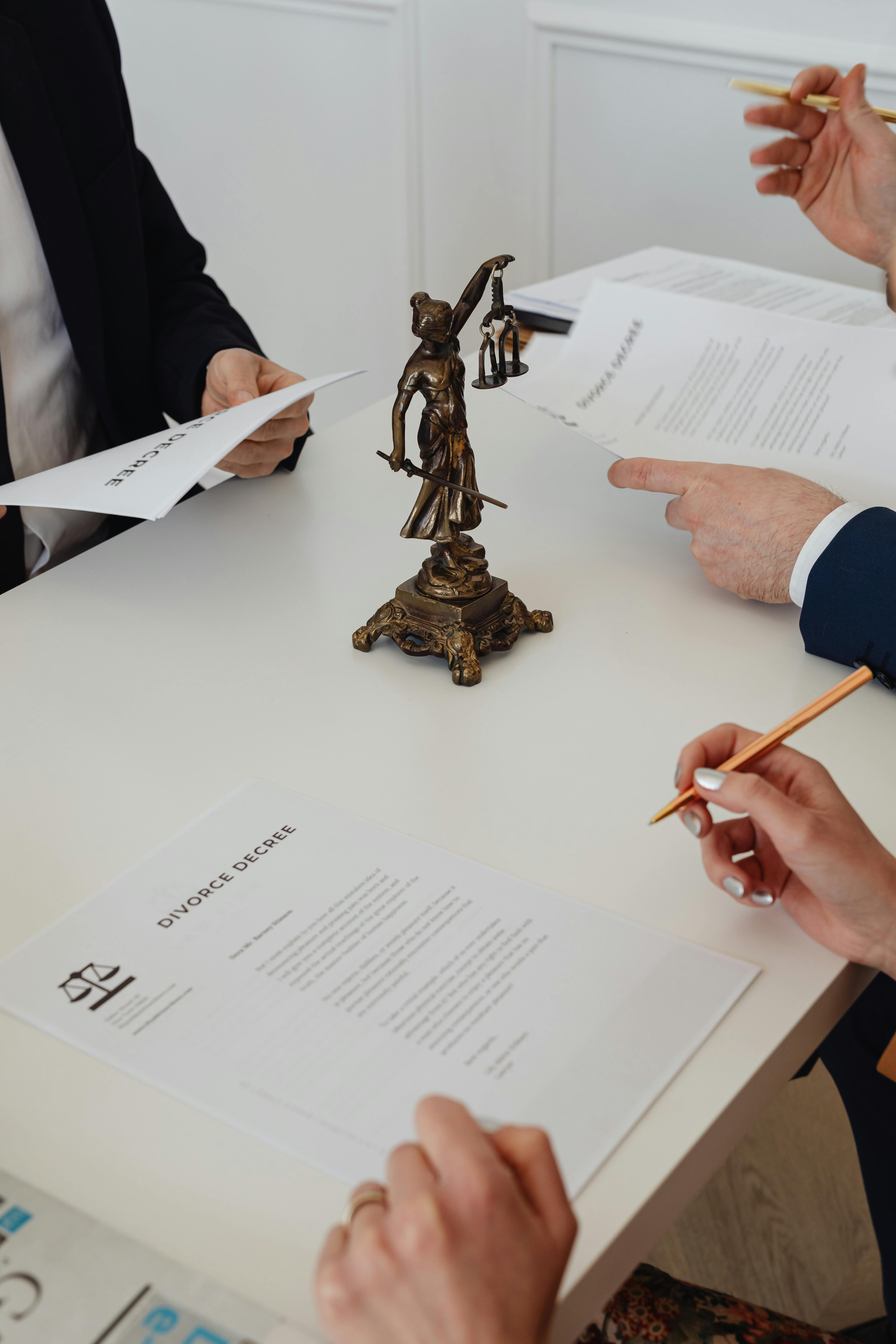 Multiple people around a table reviewing divorce decree documents with a Lady Justice statue in the center