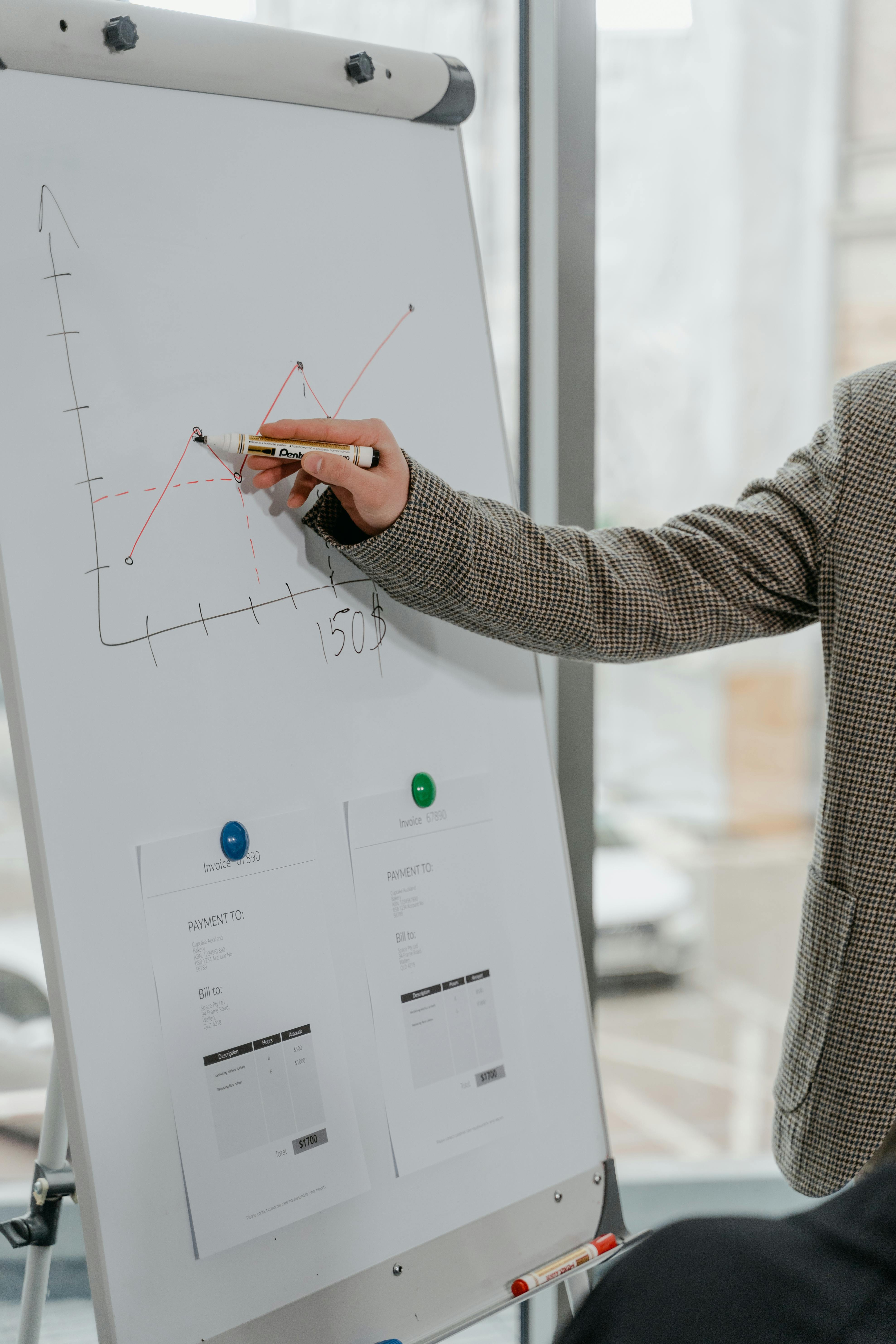 Person in a suit drawing an upward line graph on a whiteboard with printed documents displayed