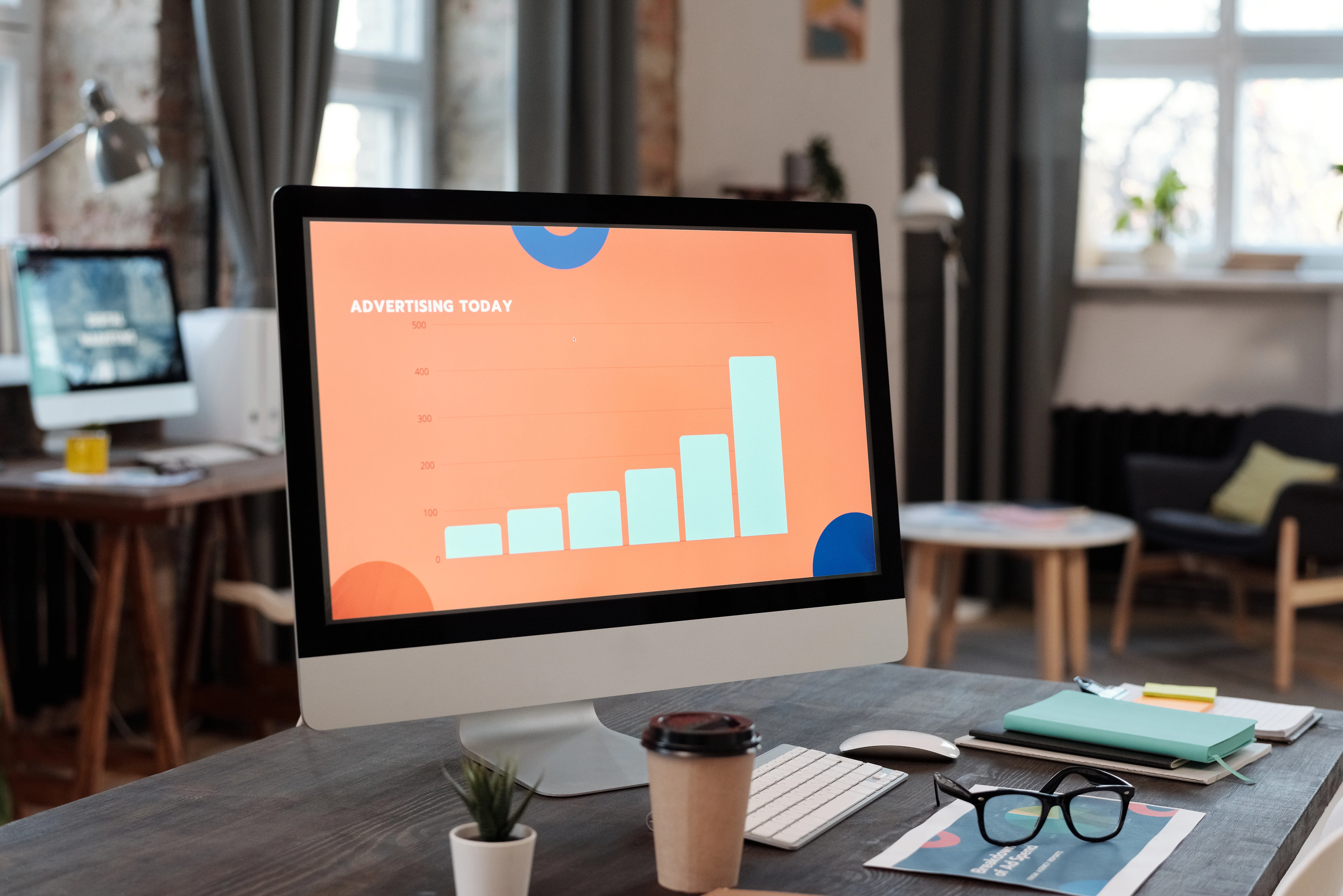 Desktop monitor displaying an advertising bar chart presentation in a creative office