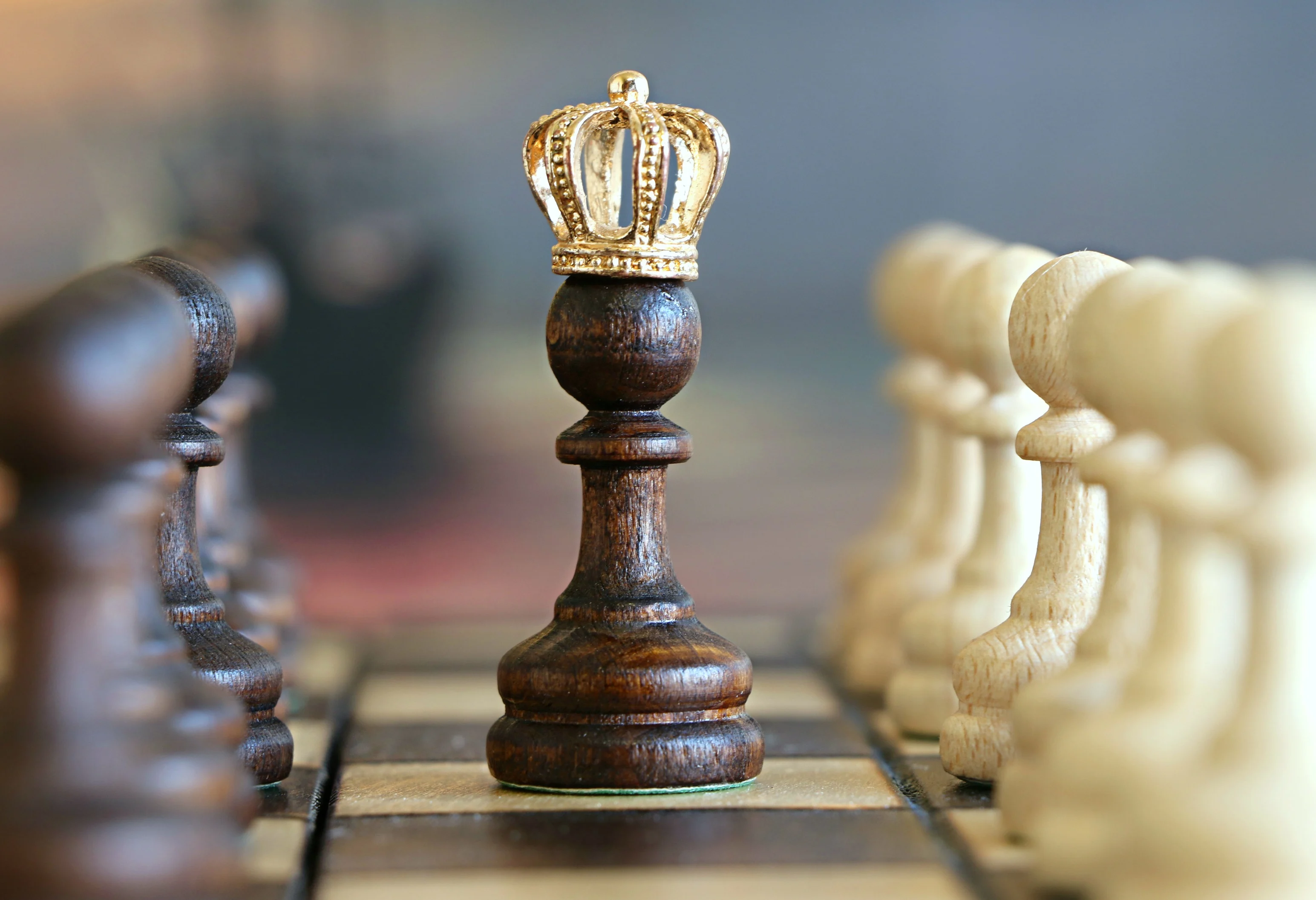 Dark wood chess pawn wearing a gold crown standing among other chess pieces on a board