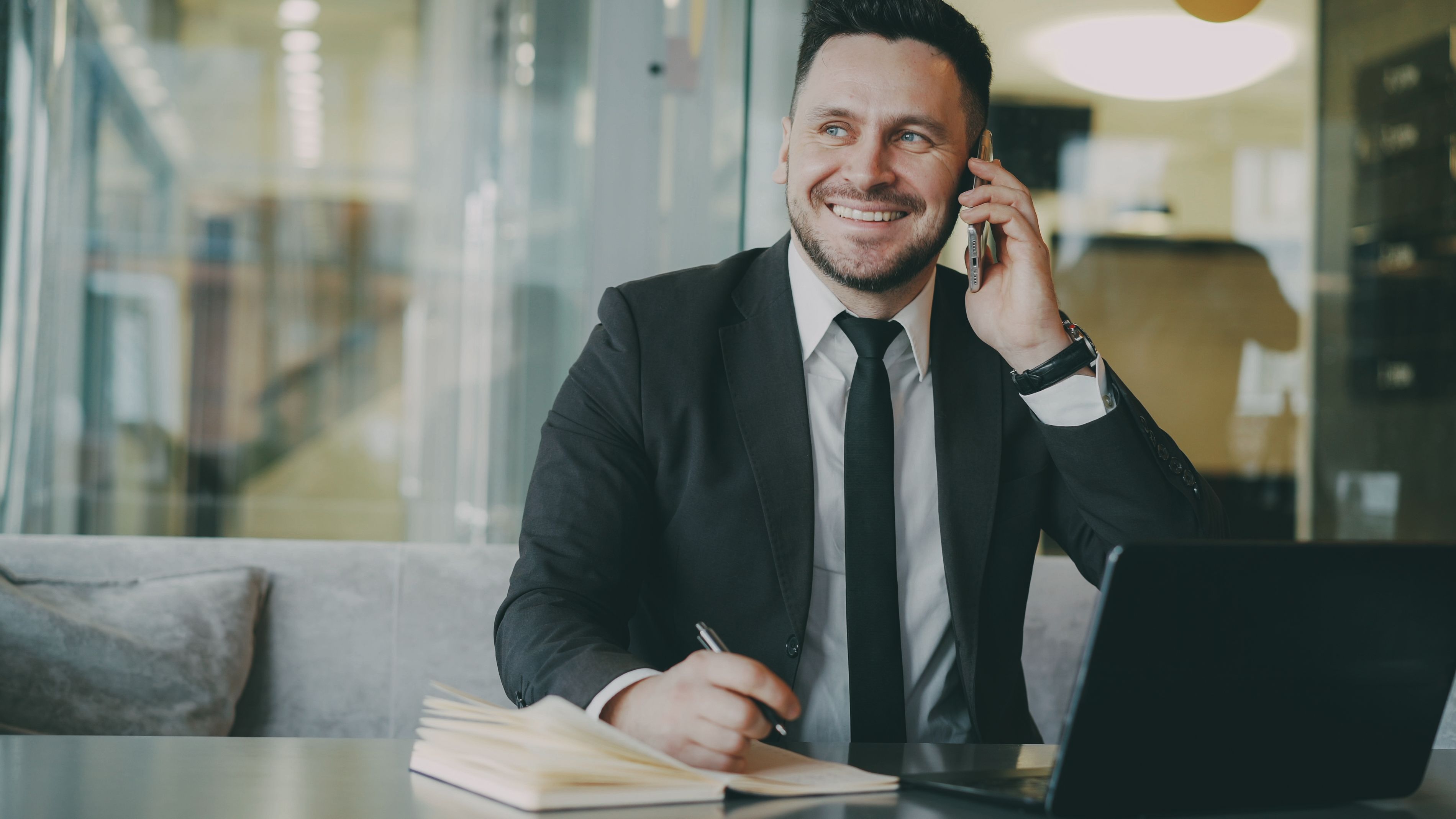 Attorney in a suit smiling while on the phone and taking notes at his desk