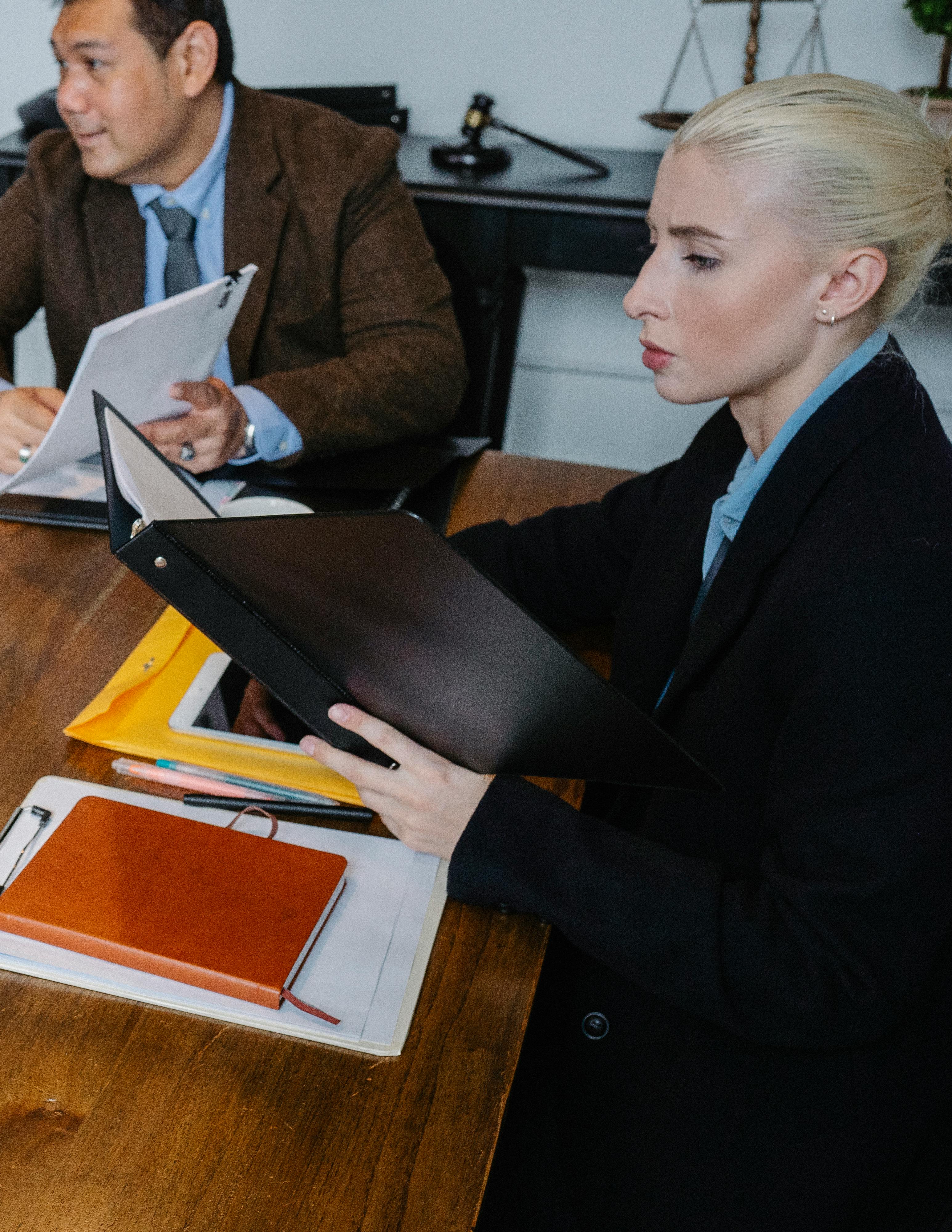 Female attorney reviewing a binder in a law office while a male colleague sits at the table in the background