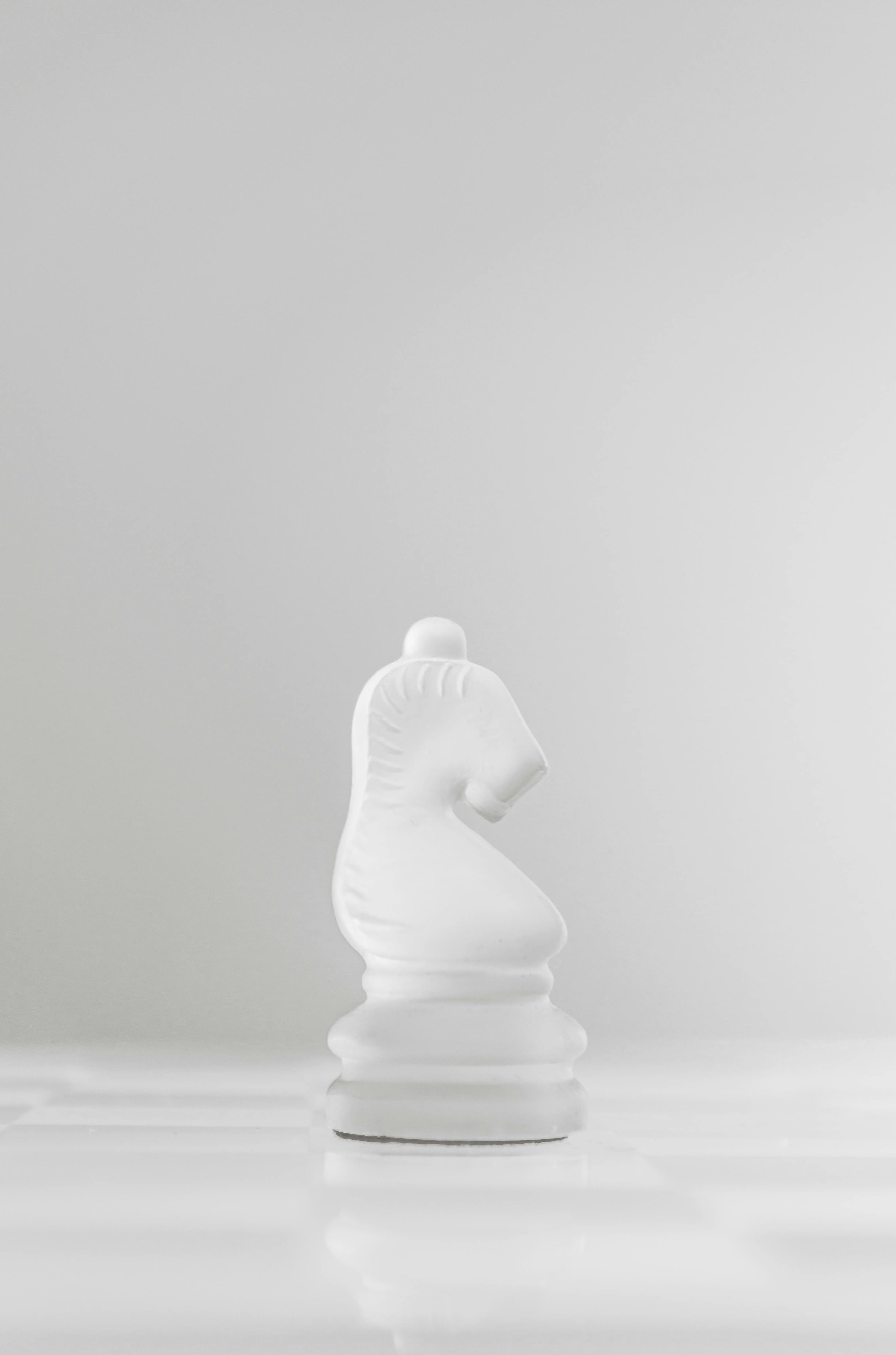 White chess knight piece standing alone on a white reflective surface against a light grey background